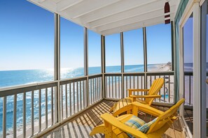 Un balcon avec vue sur l’océan, agrémenté de chaises jaunes et d’un plancher en bois.