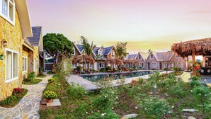 A resort with stone buildings, a swimming pool, and lush gardens.
