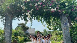 A group of people posing under a floral archway in a garden setting.