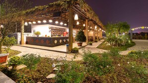 A restaurant with a thatched roof, outdoor seating, and a well-lit patio area.