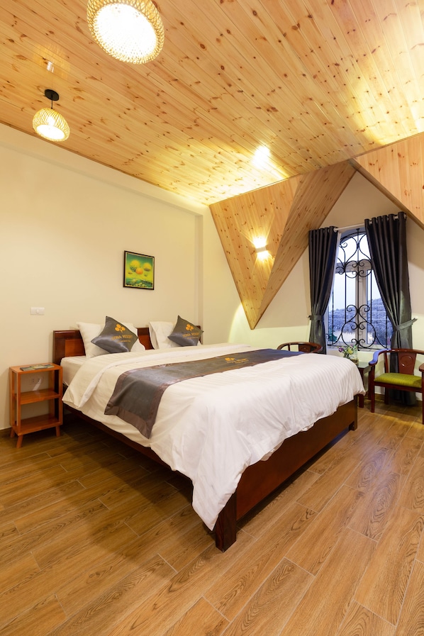 A bedroom with a wooden ceiling, a bed with white bedding, a bedside table, a chair, and a window with curtains.