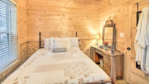 Quarto de cabana de madeira com cama, cômoda, espelho e janela.