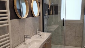 Ein modernes Badezimmer mit zwei Waschbecken, einer Duschkabine aus Glas und einem gemusterten Boden.
