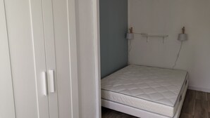 Ein Schlafzimmer mit einem weißen Kleiderschrank, einer weißen Matratze und einem an der Wand befestigten Regal mit zwei Lampen.