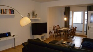 A living room with a black leather sofa, a flat-screen TV, a dining table with chairs, and a bookshelf. - Unique Maisonette Suite for 6 people, Refurbished Historical Villa! Nice Price!! (Bad Salzuflen)