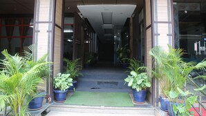 A hotel entrance with a covered walkway, potted plants, and a green mat.