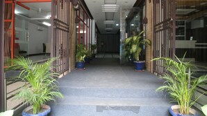 A hallway with steps leading to a door, flanked by potted plants and a glass door on the right.