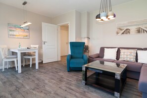 Una sala de estar moderna con sofá, una mesa de centro, un sillón azul y un comedor con mesa y sillas.