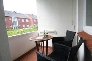 Un balcon avec une petite table et deux chaises en osier, donnant sur un quartier résidentiel avec des immeubles en briques.