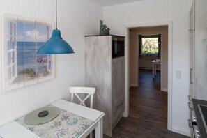 Una cocina con un armario blanco, una lámpara colgante azul y vistas al mar a través de una ventana.