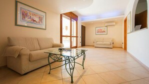 Un salon spacieux avec une table basse en verre, deux canapés et un grand tableau accroché au mur.