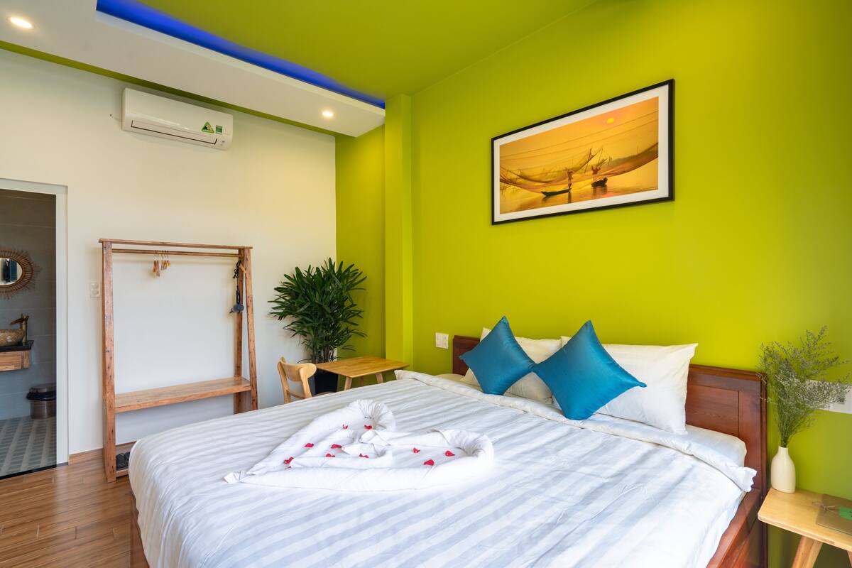Ein Hotelzimmer mit einem Bett, einem hölzernen Kopfstück, einem Gemälde an der Wand und einem kleinen Tisch mit einer Pflanze.