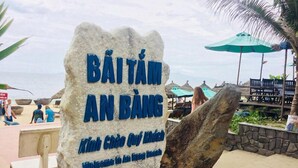 A stone sign with 'BÁI TÁM AN BÁNG' and 'Welcome to An Bánh' written on it, indicating a beach area. - Homestay An Bang Sea Adventure (Da Nang)
