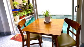 A dining area with a wooden table and chairs, a potted plant, and a view of a swimming pool through a glass door. - Homestay An Bang Sea Adventure (Da Nang)