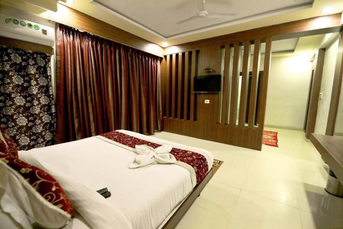 Una habitación de hotel con una cama, cortinas, un televisor y una pared de paneles de madera.