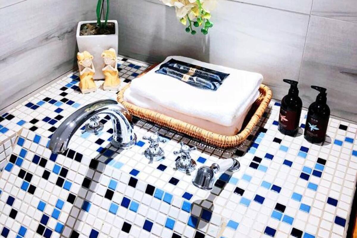 Un baño con suelo de baldosas, un lavabo, un espejo, una toalla y una botella de champú.