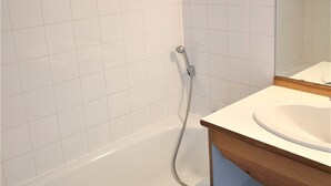 Ein Badezimmer mit weißen Fliesen, einer Dusche und einem Holzkosmetikschrank mit Waschbecken.