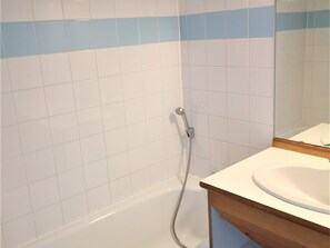 A bathroom with white tiles, a shower, and a wooden vanity with a sink.