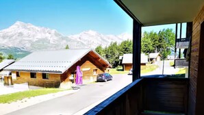 Eine Bergingerhütte mit Holzfassade, einem Balkon mit Blick auf die Straße und die Berge, und einem geparkten Auto davor.