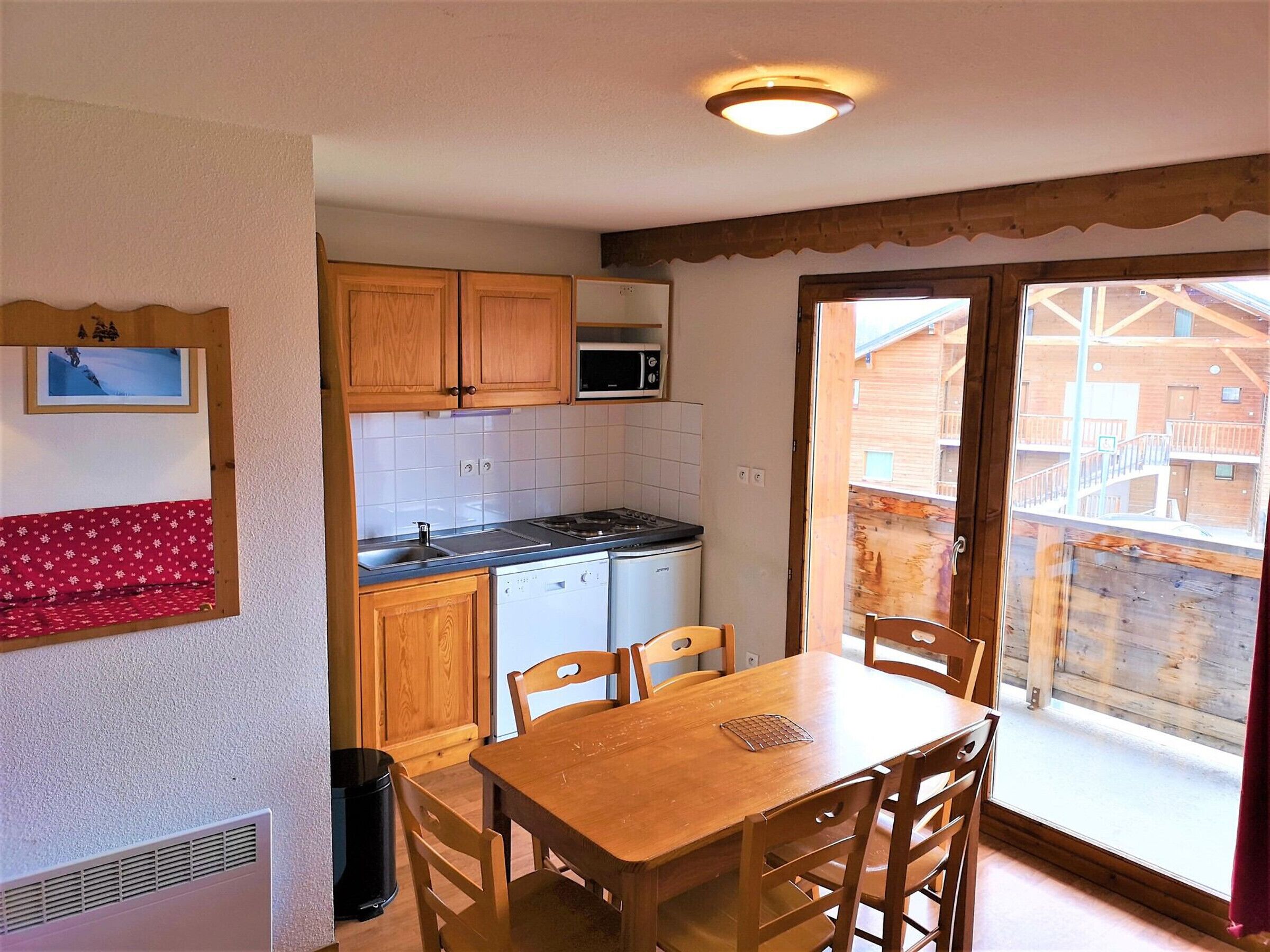 A kitchen with wooden cabinets, a microwave, and a dishwasher. There is a dining table with chairs and a window with a view of a wooden building outside.
