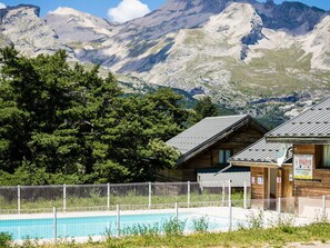Eine Holzhütte mit Pool, umzäunt und mit Bergen im Hintergrund.