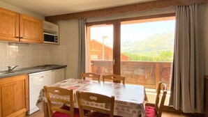 Eine Küche mit Holzausstattung, einer Mikrowelle und einem Geschirrspüler. Es gibt einen Esstisch mit Stühlen und einen Blick auf Berge durch das Fenster.