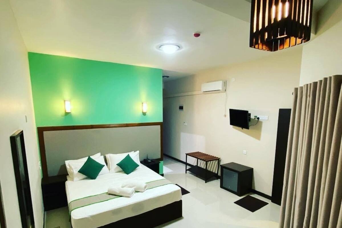 A modern hotel room with a large bed, bedside tables, a TV, and a ceiling light fixture.