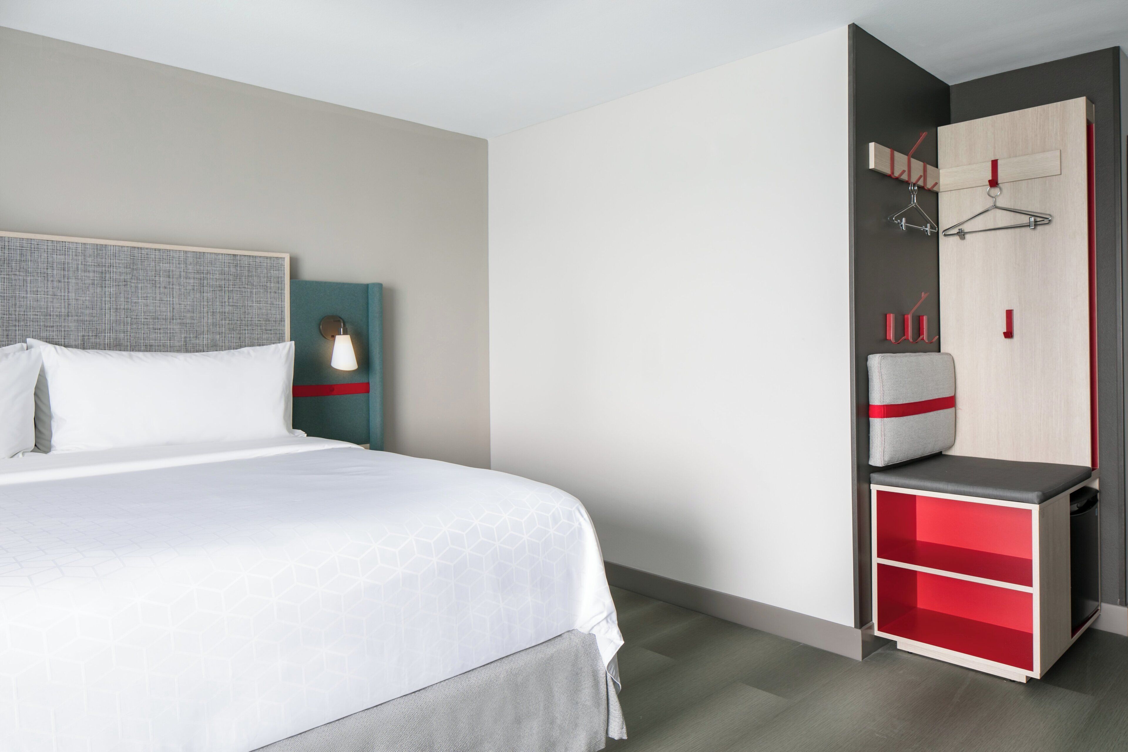 Una habitación de hotel con cama, mesita de noche, armario y perchero.