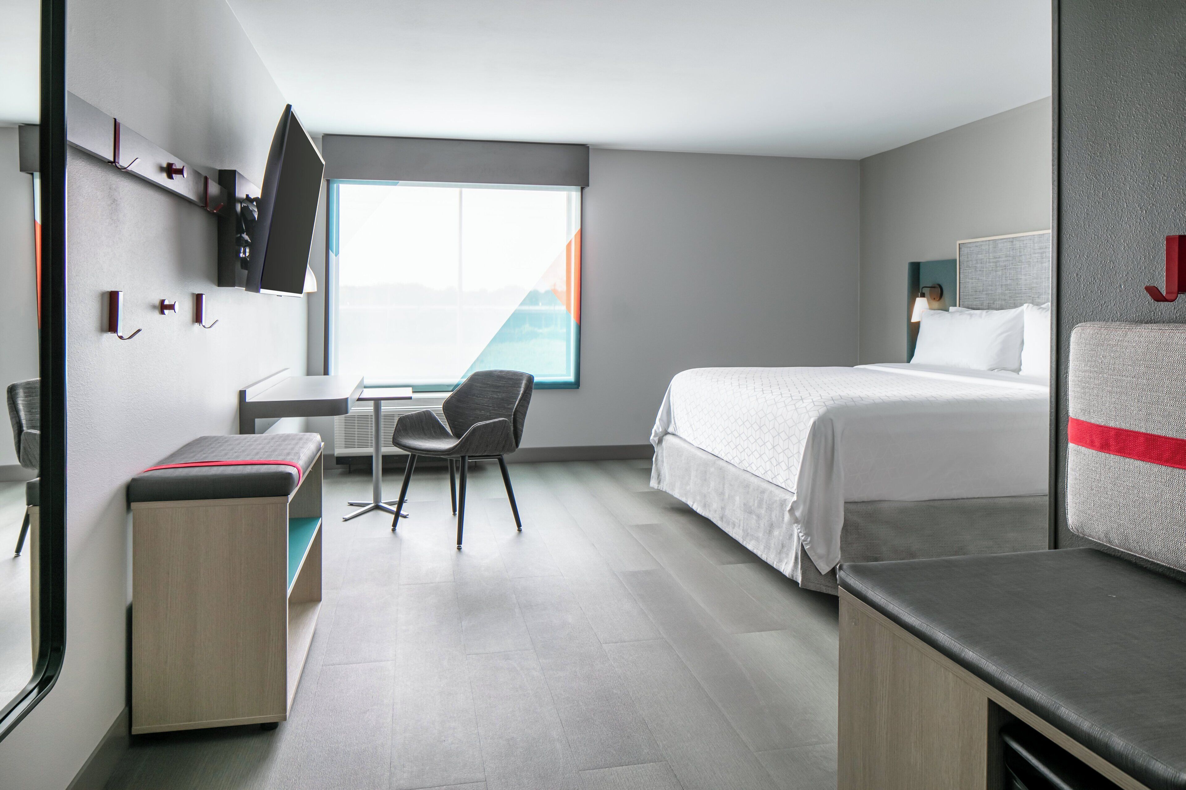 A hotel room with a bed, a desk, a chair, a TV, and a window with a view.