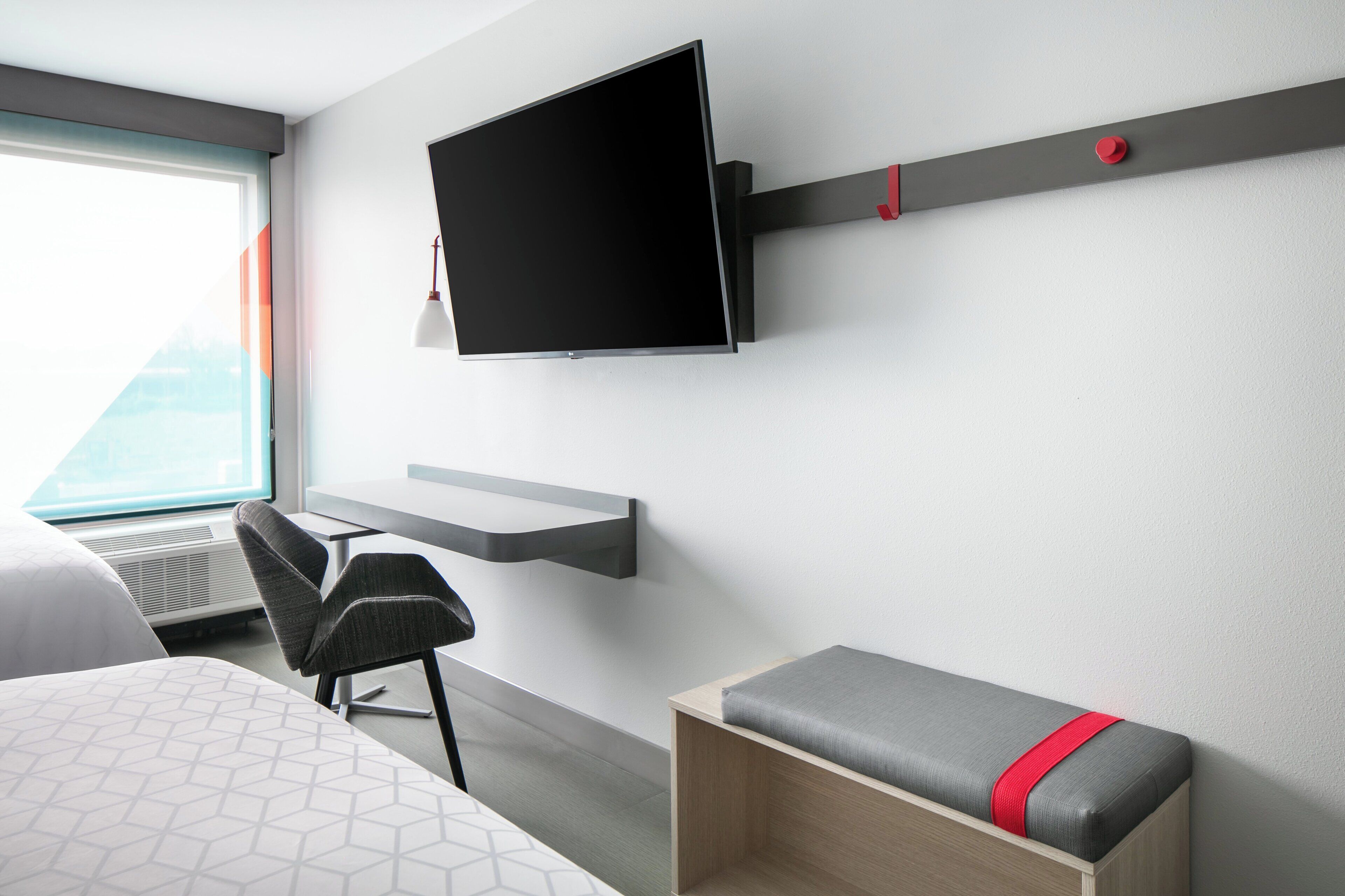 Une chambre d’hôtel équipée d’un lit, d’un bureau, d’une chaise, d’un téléviseur fixé au mur et d’une fenêtre donnant sur un paysage agréable.
