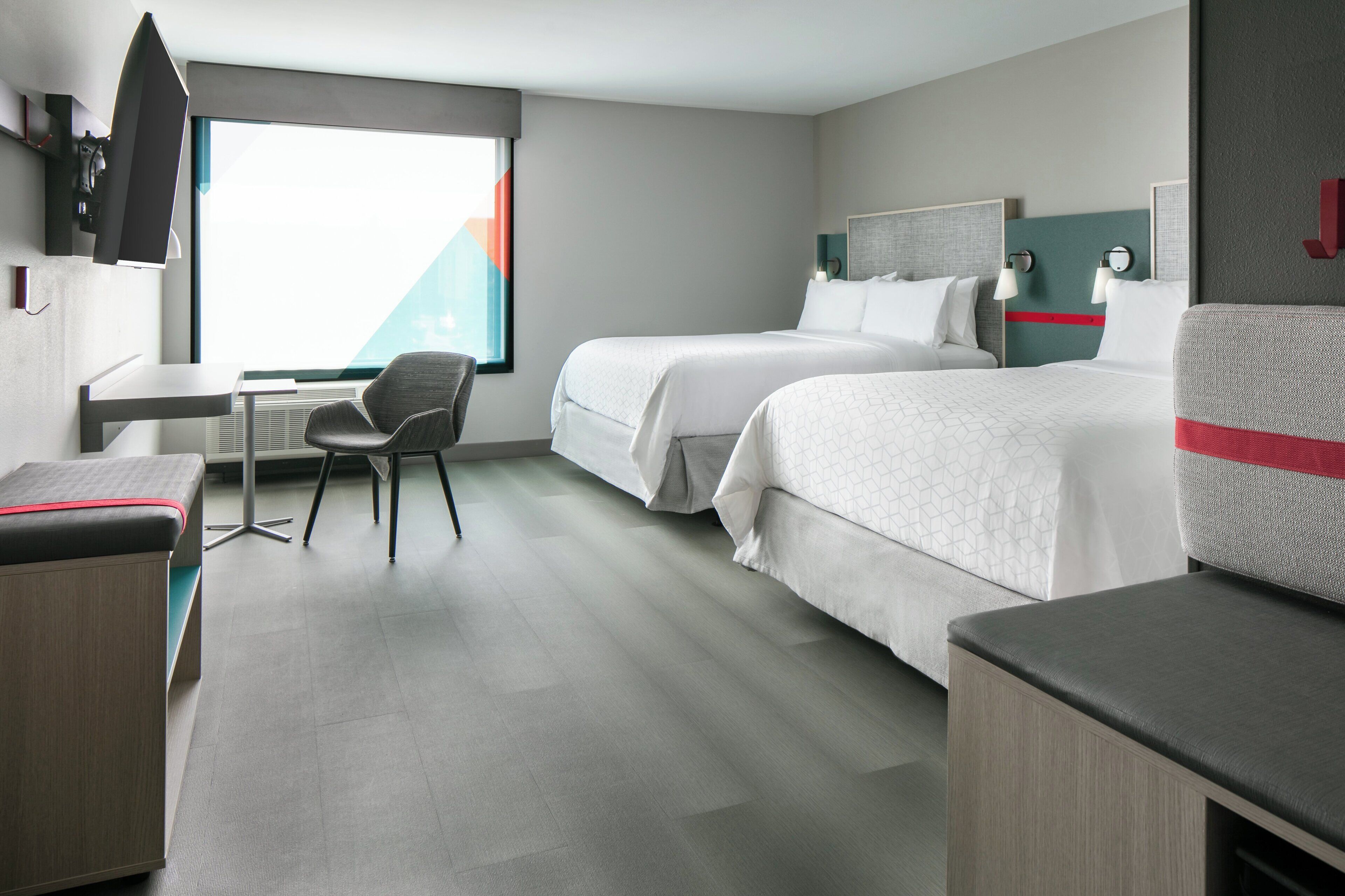 A hotel room with two beds, a desk, a chair, and a large window.