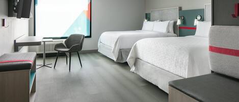 Habitación de hotel con dos camas, un escritorio, una silla y un ventanal amplio.