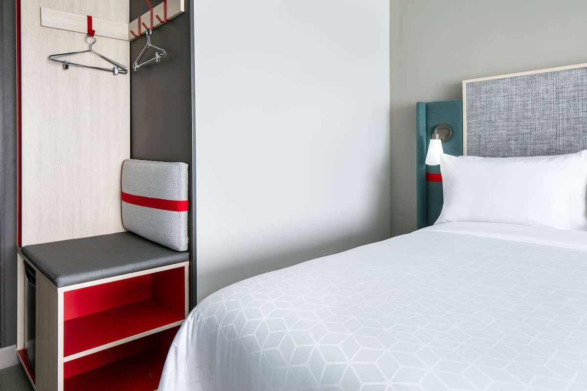 Ein Hotelzimmer mit einem Bett, einer roten und grauen Bank, einem Kleiderschrank und einer Wandlampe.