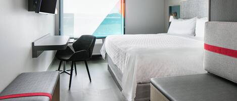 Una habitación de hotel con cama, escritorio, silla y banco.