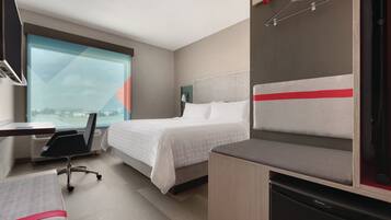 A hotel room with a bed, a desk, a chair, a small table, and a view of the city.