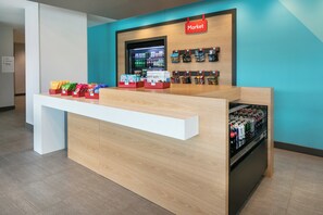 A reception desk with a 'Market' sign above, snack dispensers, and a refrigerated display of beverages. - avid hotel Roseville - Minneapolis North by IHG (Roseville)