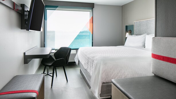 A modern hotel room with a bed, a desk, a chair, and a bench. - avid hotel Roseville - Minneapolis North by IHG (Roseville)