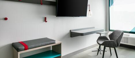 A modern room with a mounted TV, a bench with a red accent, a chair, and a window with a view.