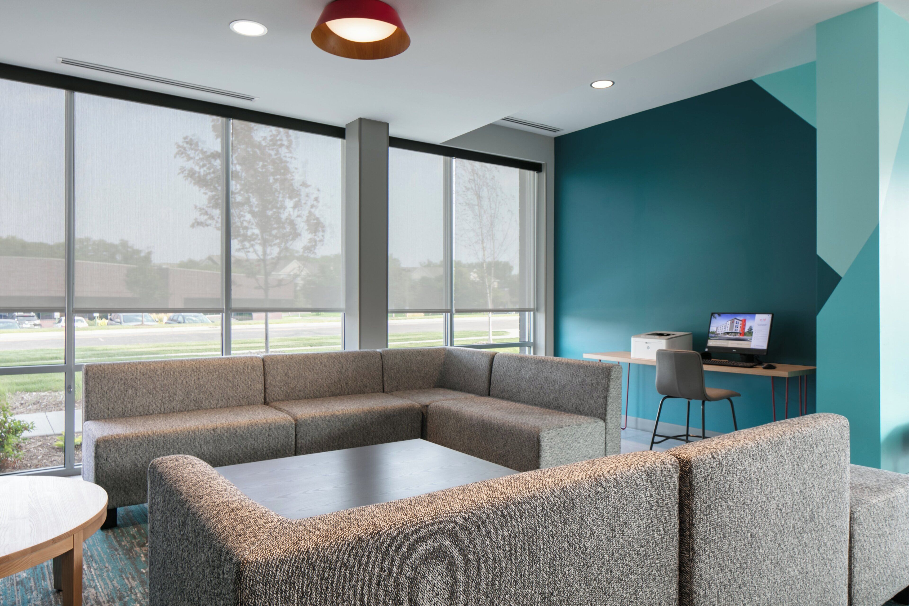 Un espace de bureau moderne comprenant un canapé d’angle, une table basse et un bureau avec un ordinateur.
