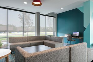 A modern office space with a sectional sofa, a coffee table, and a desk with a computer. - avid hotel Roseville - Minneapolis North by IHG (Roseville)