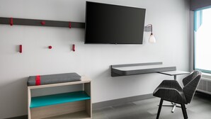 A modern room with a flat-screen TV mounted on the wall, a small table, a chair, and a bench with cushions. - avid hotel Roseville - Minneapolis North by IHG (Roseville)