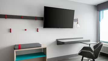 A modern room with a flat-screen TV mounted on the wall, a small table, a chair, and a bench with cushions.