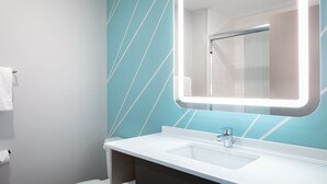 A modern bathroom with a white sink, a large mirror with LED lighting, and a teal patterned wall. - avid hotel Roseville - Minneapolis North by IHG (Roseville)