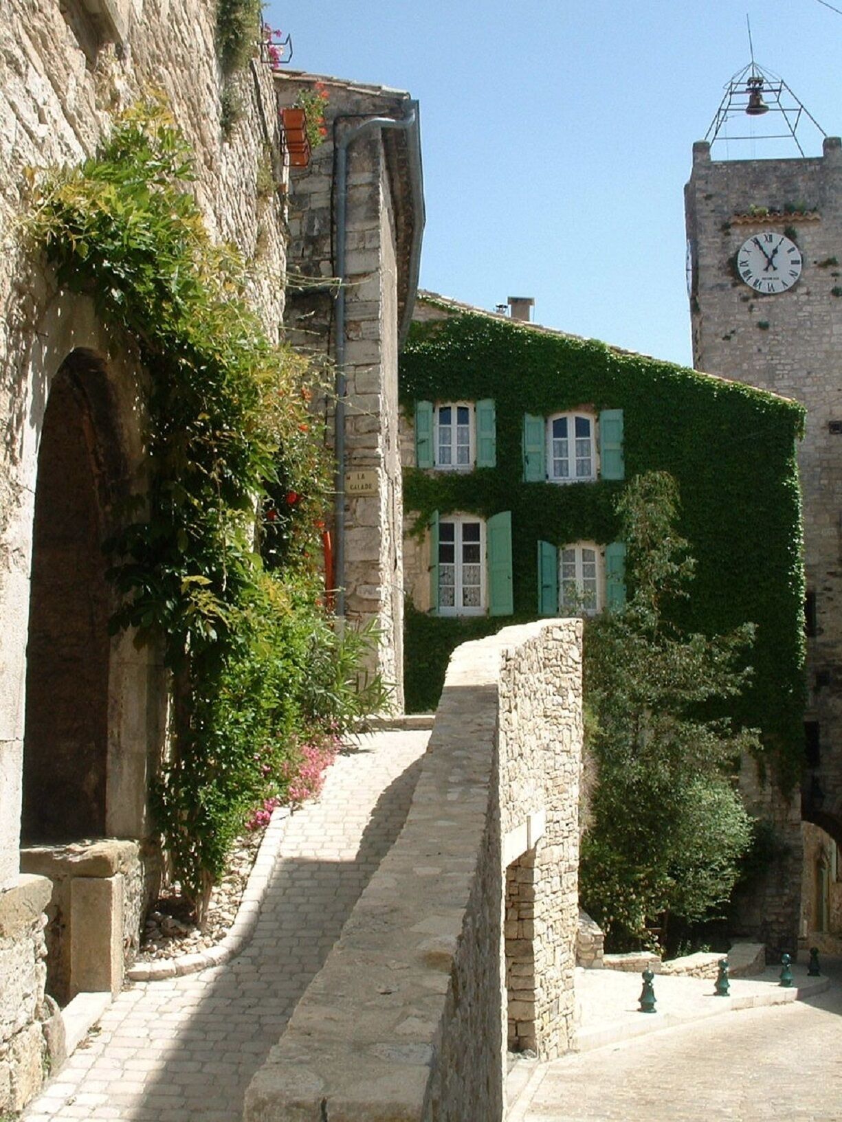 Uma escadaria de pedra leva a um edifício com venezianas verdes e uma torre do relógio.