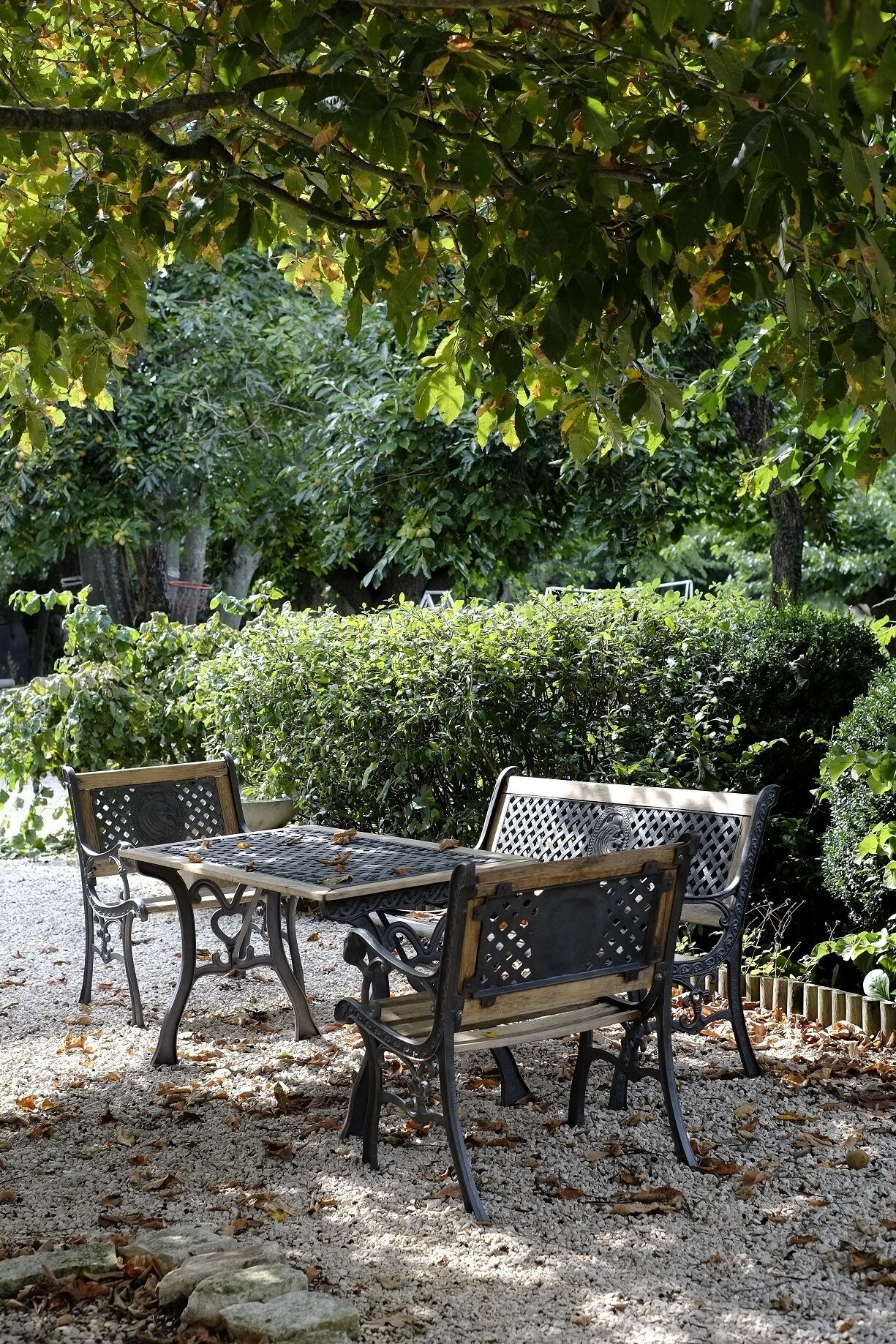 Un espace extérieur aménagé avec deux chaises en métal et une table, entouré de gravier et d’un sol recouvert de feuilles, sous un arbre.