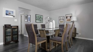 A dining area with a glass-top table surrounded by chairs, framed artwork on the walls, and a bookshelf with books. - Spectacular Views, Single Level w/ Huge Deck & BBQ, Pet Friendly, Next to Forest Park Hiking Trails (Portland)