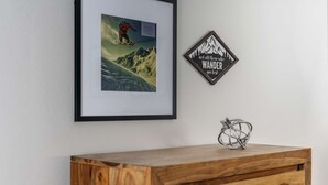 A framed picture of a snowboarder on a mountain, a diamond-shaped sign with the text "not all those who WANDER are lost," and a wooden cabinet with a metal sculpture on top. - Spectacular Views, Single Level w/ Huge Deck & BBQ, Pet Friendly, Next to Forest Park Hiking Trails (Portland)