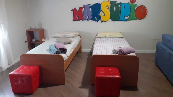 A room with two beds, each with a red bench, a small table with a lamp, and a colorful wall sign. - OPEN (Potenza)