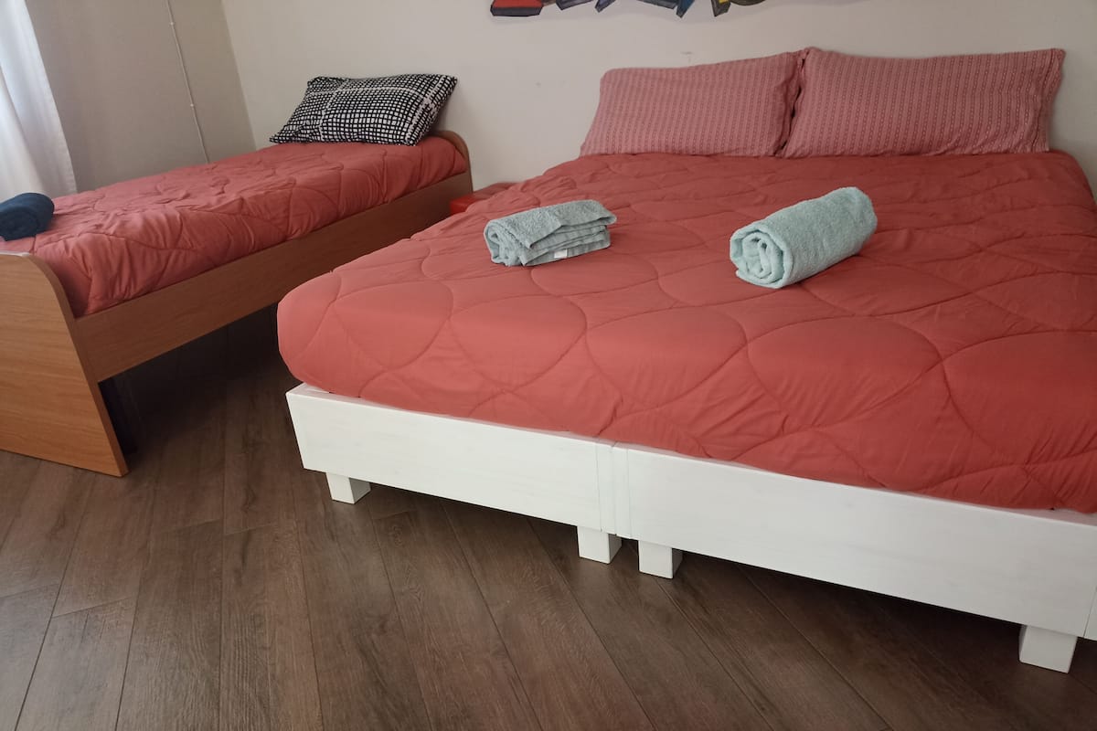 Un dormitorio con una cama grande, una cama más pequeña y una mesita de noche de madera.
