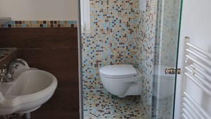 Une salle de bain avec une paroi de douche carrelée, des toilettes et un lavabo avec un robinet.